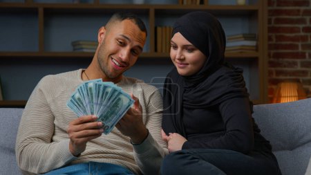 Photo for Rich muslim woman and african american man owners hold cash dollars planning family budget win money in lottery smiling interracial ethnic couple earning finance receive credit for house loan mortgage - Royalty Free Image