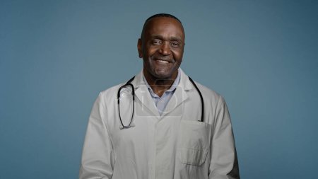Téléchargez les photos : Mature african american man doctor stand in blue background studio in protective mask in medical gown takes off respirator breathe sigh relief breathing deeply feels happy and healthy recovery concept - en image libre de droit