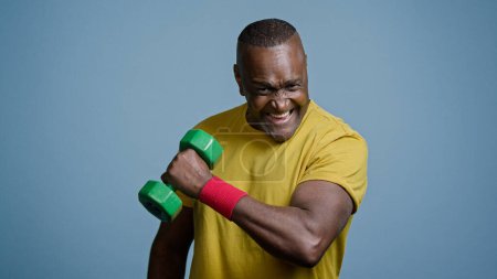 Foto de Mature strong athletic man coach pumping biceps with dumbbell in studio on gray background doing exercise pumps up muscles using sports equipment healthy athlete sportsman enjoys great workout result - Imagen libre de derechos
