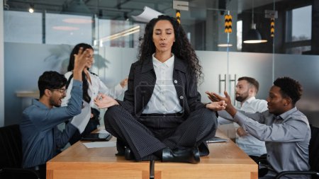 Calma mujer de negocios profesional tomando descanso meditando sentado en la mesa en la reunión de la oficina ignorando a los colegas ruidosos discutiendo lluvia de ideas argumentar consciente jefe femenino saludable haciendo yoga sin estrés zen