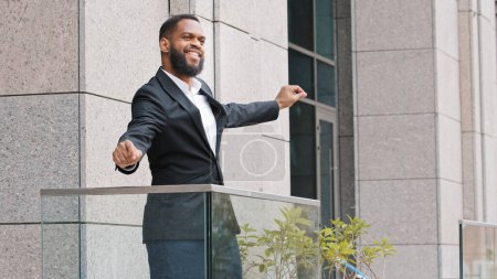 Téléchargez les photos : Heureux drôle joyeux Africain ethnique américain employé masculin ayant plaisir entrepreneur homme d'affaires travailleur homme sur le bureau balcon danse célébrer le succès de l'entreprise gagner le succès de l'entreprise avec la danse - en image libre de droit