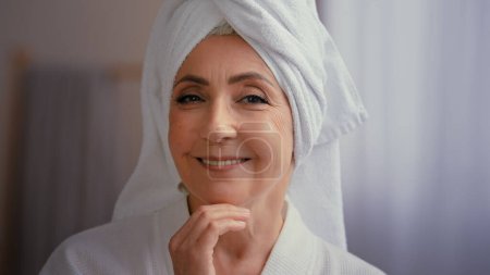 Photo for Cheerful female portrait happy 50s middle-aged lady 60s mature woman touching facial skin looking at camera with smile touch face pampering wears towel on head enjoy cosmetics and plastic surgery - Royalty Free Image