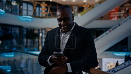 Téléchargez les photos : Afro-américain homme d'affaires debout dans le centre commercial bureau de l'entreprise homme regardant parler téléphone mobile a conférence téléphone intelligent vidéo parler discuter amical sourire répondre téléphone portable chat - en image libre de droit