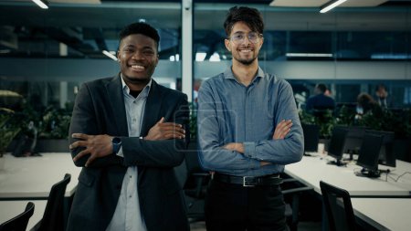 Foto de Compañeros de negocios multirraciales sonriendo diversos hombres empresarios árabes y africanos compañeros de trabajo empleados de pie en la oficina juntos posando brazos cruzados retrato exitoso hombres personas corporativas trabajo en equipo - Imagen libre de derechos