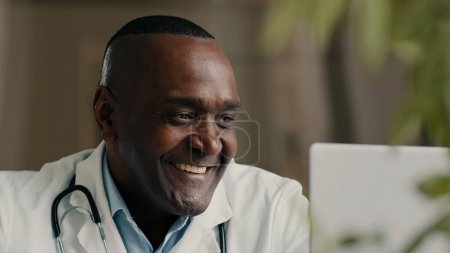 Téléchargez les photos : Médecin psychothérapeute africain homme d'âge moyen médecin généraliste parlant avec le patient en ligne vidéoconférence webcam virtuelle chat app medic consulting remote during corona virus pandemic - en image libre de droit