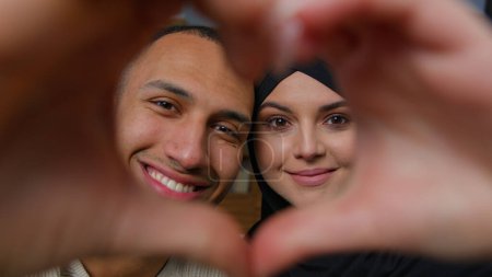 Téléchargez les photos : Newlyweds diverse ethnic married couple african american man with beloved arabian woman looking at camera through heart frame united husband wife hands in love shape Valentines Day romantic relation - en image libre de droit