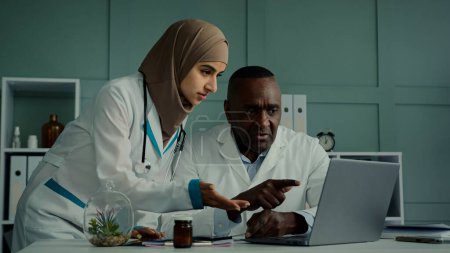 Téléchargez les photos : Médecins multiraciaux collègues discutent travail d'équipe homme africain et femme arabe deux professionnels de la santé parlent de soins de santé vérifier IRM scanner utiliser une application informatique faire des recherches en ligne X-ray résultats - en image libre de droit