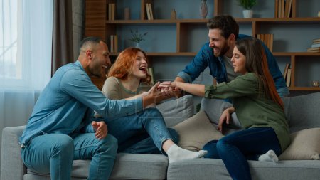 Foto de Group friends ethnic diverse women and men multiracial companions business people sit on sofa discuss plans talk indoors approve cooperation stacking hands together in pile team gesture unity teamwork - Imagen libre de derechos