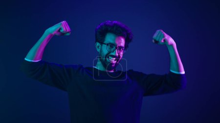 Photo for Funny Indian man slim guy fooling around show hands muscle biceps sport strong power bodybuilder ultraviolet neon studio background proud champion boast efficient security coding achievement level up - Royalty Free Image