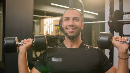 Photo for Happy smiling African American sportsman doing power exercise at gym with sport equipment bodybuilder man lifting heavy weights dumbbells workout male fitness athlete training shoulders hands muscle - Royalty Free Image