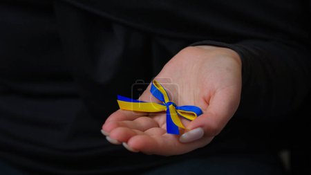 Téléchargez les photos : Gros plan mains féminines méconnaissables tenir le ruban bleu jaune femme inconnue dame dame palmiers volontaires tenant symbole ukrainien debout avec l'Ukraine protection charité soutenir les victimes de la guerre vue recadrée - en image libre de droit