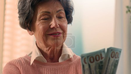 Téléchargez les photos : Heureux sourire riche Caucasienne vieille femme compter de l'argent à la maison factures gagner bonus grand-mère compter les dollars senior mamie tenant de l'argent vieille femme âgée dame à la retraite avec des billets de banque épargne financière - en image libre de droit