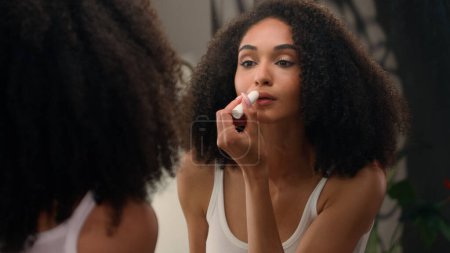Téléchargez les photos : Belle femme afro-américaine regardant dans miroir reflet matin beauté routine préparation ethnique fille dans la salle de bain application hydratant rouge à lèvres rouge à lèvres lèvres lisses cosmétiques naturels biologiques - en image libre de droit