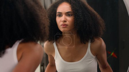Photo for Worried young beautiful African American woman sad ethnic girl looking in mirror stressed about facial wrinkles problem acne frustrated upset touching face dry sensitive skin care facial blackheads - Royalty Free Image