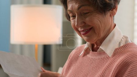 Foto de Caucásica anciana mujer mayor señora jubilada abuelita madura abuela abierta papel carta postal leer texto recibido buenas noticias de la familia leyendo aviso bancario sonrisa feliz en el sofá de casa - Imagen libre de derechos