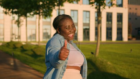 Foto de Entusiasta feliz éxito afroamericano estudiante étnico mujer satisfecha al aire libre ciudad mostrando como pulgar arriba consentimiento aprobación de acuerdo como gesto de la mano acuerdo de apoyo signo recomiendan sonreír - Imagen libre de derechos