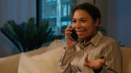 Photo for Smiling African American ethnic woman talk mobile phone order food delivery listen good news emotional talking on couch excited female girl businesswoman carefree business conversation at evening home - Royalty Free Image