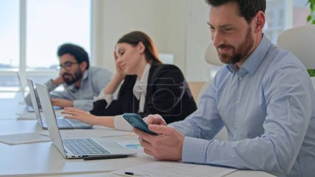 Photo for Multiracial business employees unmotivated staff sit at corporate office distracted from boring laptop job play mobile phone game tired bored lazy businessmen businesswoman feel low energy fall asleep - Royalty Free Image
