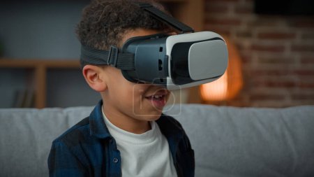 Photo for Little African American funny boy pupil son kid child schoolboy at home play video game wearing VR glasses playing online 3d fight pretend fighting with augmented virtual reality headset AR metaverse - Royalty Free Image