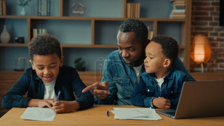 Photo for Single parent African American father man babysitter private teacher with two boys kids children help little schoolboy son child boy with school homework teaching writing task distant home education - Royalty Free Image