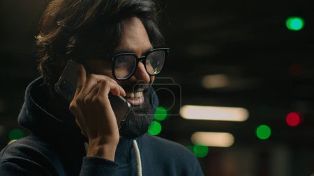 Foto de Primer plano barbudo indio hombre en gafas en el estacionamiento sonriente árabe hombre adulto chico en gafas hombre de negocios hablar teléfono risa sonrisa agradable negocio llamada hablar conversación móvil en metro - Imagen libre de derechos