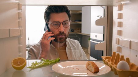 Photo for Point of view POV inside refrigerator Caucasian male man guy open fridge with one egg lettuce leaf piece of bread crumbs empty bottle of juice talking phone order products call food delivery service - Royalty Free Image