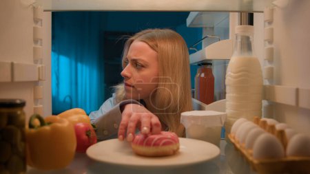 Photo for Point of view POV from inside refrigerator hungry woman girl at night kitchen open fridge looking around eating bite sweet donut unhealthy nutrition diet failure weight control obesity food addiction - Royalty Free Image