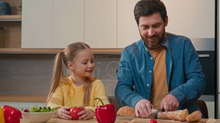 Photo for Happy family breakfast dinner lunch at home kitchen Adult father talking with cute adopted little child girl daughter cooking cut bread talk casual conversation cutting slicing baguette food delivery - Royalty Free Image
