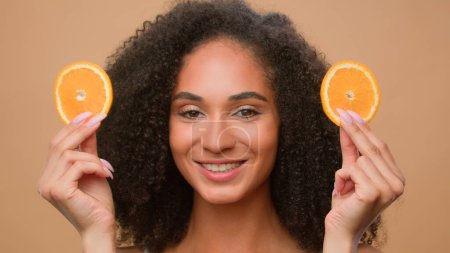 Photo for Beauty portrait African American girl woman cover eyes with two slices of orange smiling laughing diet vegetarian healthcare healthy vitamin skin face care fruit natural organic vegan citrus cosmetics - Royalty Free Image