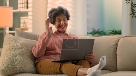 Photo for Caucasian happy cheerful old woman senior lady mature retirement granny elderly female at couch home talk laptop video chat call talking to computer web camera conference with grandchildren children - Royalty Free Image