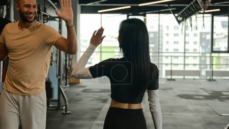 Photo for Back view sportswoman fitness trainer go through sport equipment in gym after workout unknown slim fit woman meet man sportsman give high five respect two bodybuilders multiracial athletes greeting - Royalty Free Image