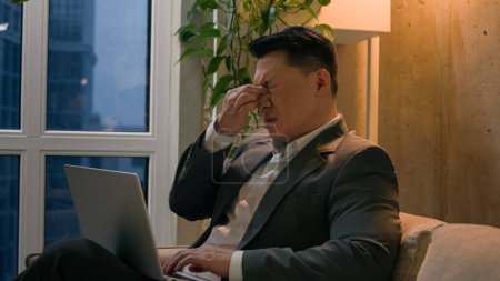 Foto de Enfermo asiático chino coreano hombre de negocios cansado hombre agotado sobrecargado de trabajo con el ordenador portátil en la oficina de la noche centro de mediana edad empresario sufren fatiga ocular dolor mala visión - Imagen libre de derechos