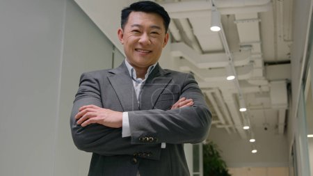 Téléchargez les photos : Homme d'affaires exécutif asiatique d'âge moyen debout dans le bureau de l'entreprise moderne. coréen chinois japonais mâle croiser les mains en regardant caméra confiant PDG propriétaire d'entreprise sourire joyeux sourire - en image libre de droit