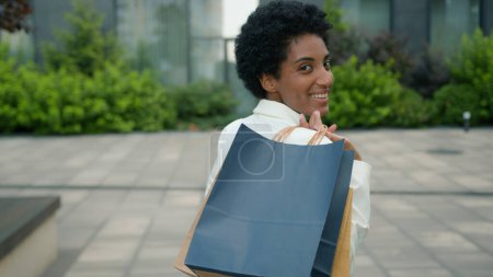 Photo for African American happy smiling woman shopper girl female buyer going customer lady client in city walking outdoors walk with shopping bags purchases goods rejoice discount sales black Friday back view - Royalty Free Image
