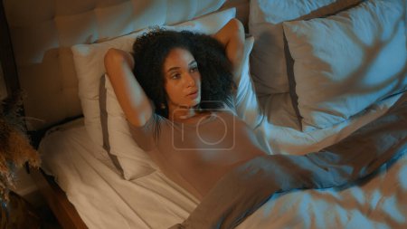Téléchargez les photos : Femme ethnique afro-américaine ennuyée couchée sur le lit dans la chambre clair de lune fille déprimée réfléchie souffrent de troubles du sommeil nuit insomnie insomnie femme trop réfléchie essayer de dormir à la maison sombre - en image libre de droit