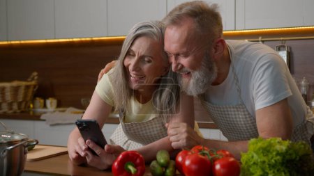 Photo for Laughing retired old gray haired Caucasian family love couple using mobile phone online order delivery food vegetables on kitchen table happy senior woman and man talking shopping cooking healthy meal - Royalty Free Image
