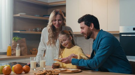 Photo for Happy Caucasian family preparing breakfast together talking at home kitchen mother hold glasses with milk little daughter child girl prepare toasts bread with chocolate pasta with father food delivery - Royalty Free Image