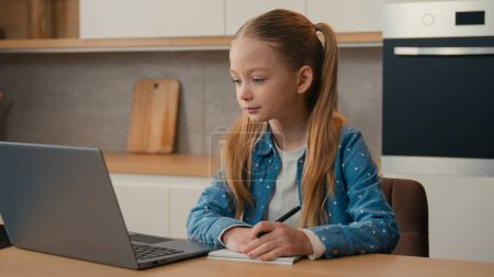 Photo for Caucasian kid girl schoolgirl listen online lesson school class distant teacher writing at home. Child pupil studying remote education with laptop video call e-learning homework write task at kitchen - Royalty Free Image