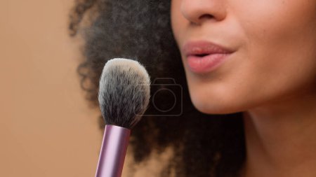 Photo for Cosmetic make-up beauty concept close-up cropped view unrecognizable African American woman unknown model girl holding brush blow away dust apply skin tone powder at beige studio background skincare - Royalty Free Image
