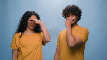 Photo for Bad smell reaction multiracial diverse couple Indian Arabian man and Hispanic woman cover noses suffer disgust stink stinky smelly aroma frowning sniffing unpleasant odor at blue studio background - Royalty Free Image