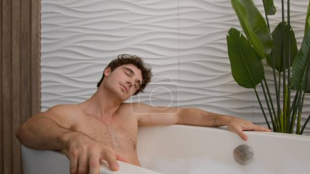 Photo for Caucasian calm tranquil relaxed man resting in warm hot bath enjoying bathing washing cleaning relaxing in warm bathtub with bubble foam male guy in shower relax in morning home hotel luxury hygiene - Royalty Free Image