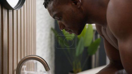 Téléchargez les photos : Bain matin routine homme afro-américain lavage visage avec verser de l'eau froide dans l'évier de salle de bains ethnique homme lavage visage propre hygiène soin hydratant rafraîchissant anti acné procédure traitement - en image libre de droit