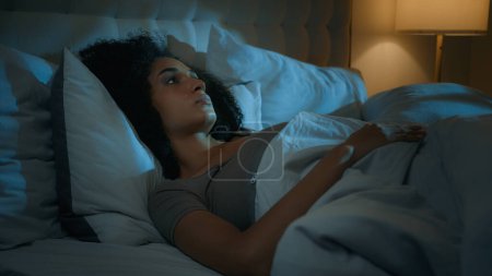 Photo for Noisy neighbours problem annoyed African American woman lying in bed night dark bedroom suffer from sleeping disorder insomnia sleepless angry girl trying sleep awake to noise cover ears with pillows - Royalty Free Image