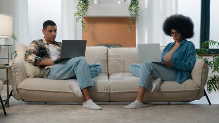 Foto de Africano americano pareja tecnología videojuego adicto familia con dos computadoras portátiles jugando en línea en sofá casa mujer trabajo con portátil hombre ordenador trabajo freelancers con computadoras en sofá separado ignorar - Imagen libre de derechos