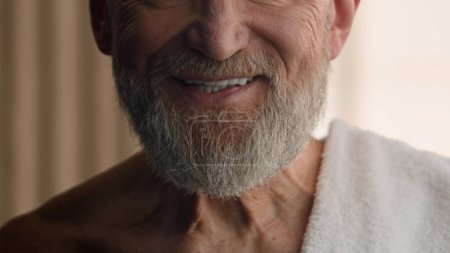 Téléchargez les photos : Gros plan recadré vue méconnaissable Caucasien vieux retraité homme barbu senior homme barbu toucher barbe grise baume toucher visage cheveux soins de la peau serviette de bain sur épaule salle de bain beauté procédure de routine - en image libre de droit