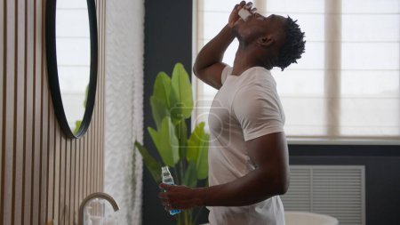 Téléchargez les photos : Afro-Américain nettoyage des dents rincer avec des produits de soins dentaires hygiène buccale à la salle de bain rinçage avec rince-bouche antibactérien haleine fraîche gargarisme liquide rafraîchissement oral matin routine quotidienne - en image libre de droit