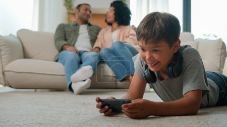 Photo for African American parents mother father talking on sofa little boy son child kid on floor play online video game on mobile phone internet addicted with smartphone happy multiracial family rest at home - Royalty Free Image