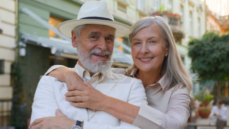 Photo for Portrait happy Caucasian family elderly couple husband wife hugging cuddle hug looking at camera outside city street. Retirement senior people enjoy romantic outdoor lifestyle vacations tour together - Royalty Free Image