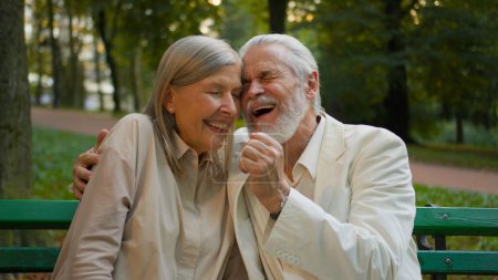 Téléchargez les photos : Gros plan portrait deux retraités âgés vieux couple caucasien assis banc rire blague câlin parlant étreignant parc de la ville à l'extérieur. Reste week-end de détente ensemble retraite insouciante grands-parents âgés - en image libre de droit