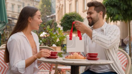 Photo for Happy European couple man gives woman a gift surprise anniversary celebration emotions city outdoors cafe together tender love feelings smiling laughter romance relationship married family enjoy care - Royalty Free Image